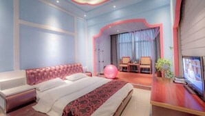Moderni hotellihuone, jossa on suuri sänky, työpöytä tietokoneella, televisio sekä oleskelualue, jossa on tuoli ja pöytä.