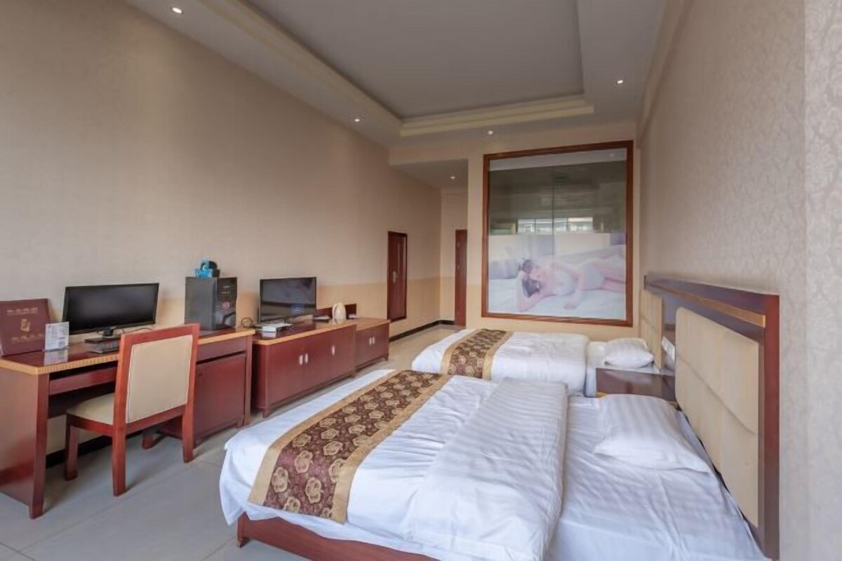 A hotel room with two beds, a desk with a computer, and a TV.