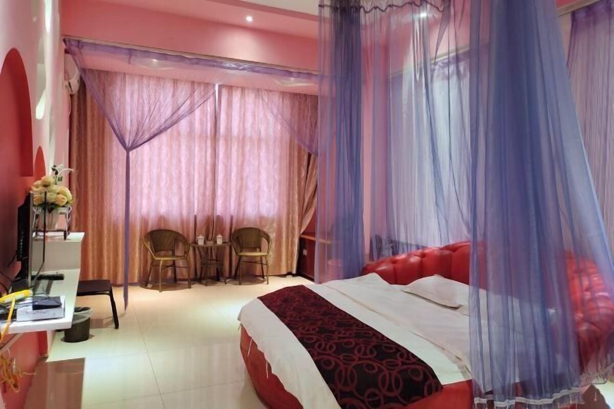 A bedroom with a red bed, a desk with a chair, and a small table with chairs.
