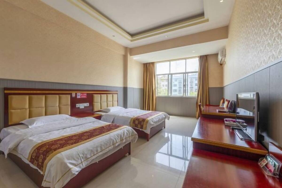 Een hotelkamer met twee bedden, een bureau, een televisie en een raam met gordijnen.