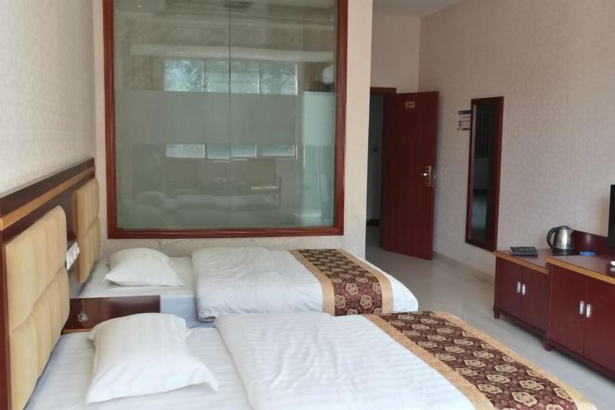 A hotel room with two beds, a large window, a wardrobe, and a mirror.