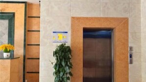 Aula, jossa on vastaanottotiski, ruukussa oleva kasvi, seinälle kiinnitetty opaste ja hissi.