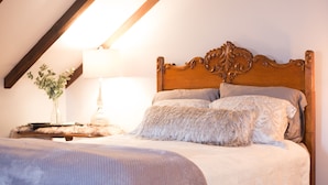 A bedroom with a wooden headboard, a bed with multiple pillows, a nightstand with a lamp, and a vase with flowers.
