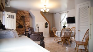 A cozy room with a brick fireplace, a dining table with chairs, a television mounted on the wall, and a staircase leading to another level.