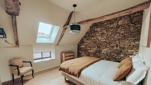 A bedroom with a stone wall, a bed with pillows, a chair, a hanging light fixture, and a skylight.