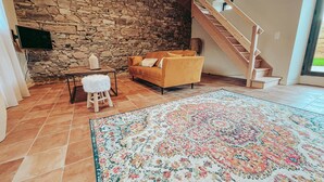 A living room with a stone wall, a wooden staircase, a sofa, a coffee table, and a patterned rug.