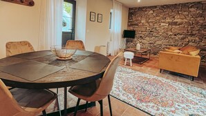 A dining area with a round table and chairs, a stone wall, a sofa, and a TV.