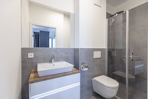 A modern bathroom with a wooden vanity, a white sink, a toilet, and a glass-enclosed shower.