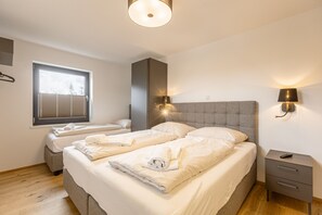 Un dormitorio con dos camas, una ventana, una mesita de noche y una lámpara de pared.