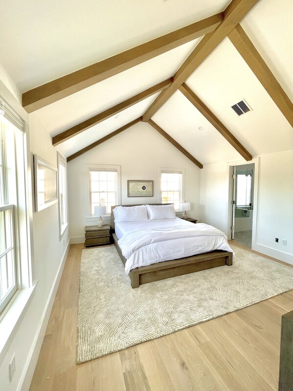 A bedroom with a sloped ceiling, wooden beams, a large bed, bedside tables, and a rug.