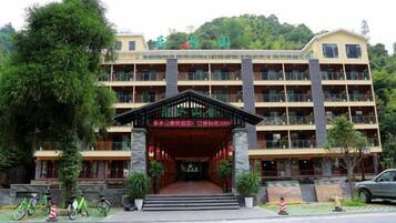 A multi-story building with a central entrance, balconies, and a surrounding green area.