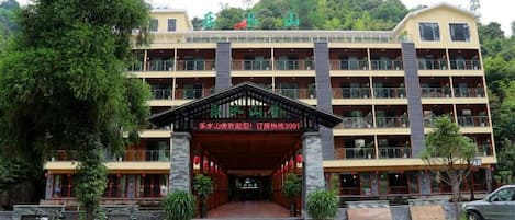 A multi-story building with a central entrance, balconies, and a surrounding green area.