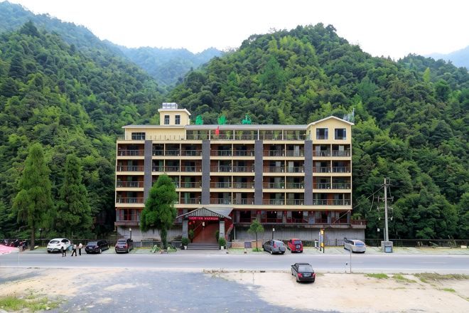 A multi-story building with a central entrance, surrounded by lush greenery and mountains.