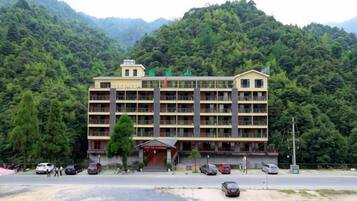 A multi-story building with a central entrance, surrounded by lush greenery and mountains.