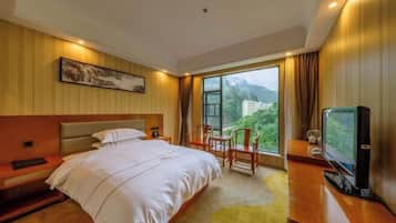 Habitación de hotel con una cama grande, un escritorio con televisor y una ventana que ofrece vistas a zonas verdes y edificios.