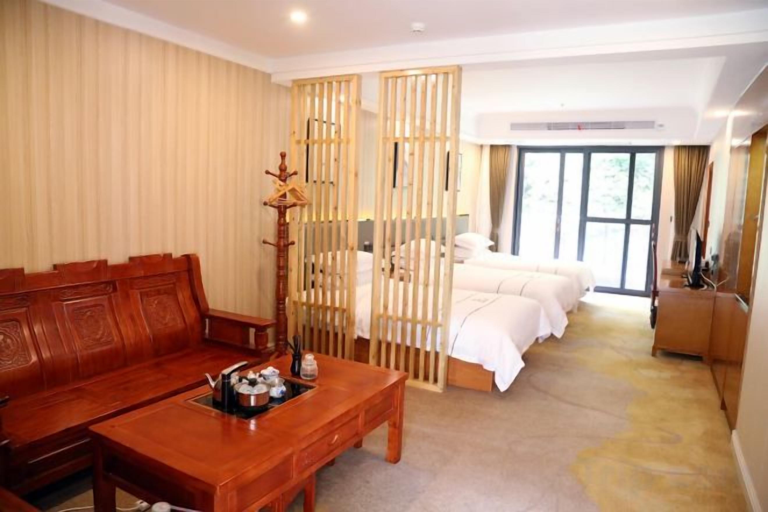 A hotel room with a wooden sofa, a small table, a bed with white bedding, and a large window.