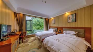 Habitación de hotel con dos camas, un escritorio con televisor, una ventana con vista a zonas verdes y un cuadro en la pared.