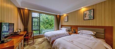 A hotel room with two beds, a desk with a TV, a window with a view of greenery, and a painting on the wall.