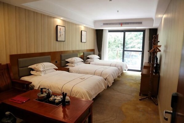 Habitación de hotel con tres camas, un escritorio de madera y vistas al exterior.