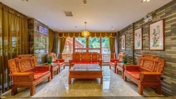 A traditional-style room with a central wooden coffee table, four wooden sofas, and a large window with a view of greenery.