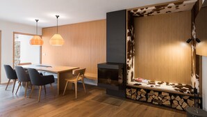 A modern kitchen with a wooden dining table, chairs, pendant lights, and a built-in wood stove. - Luxury gateway in Kranjska gora (Jesenice)