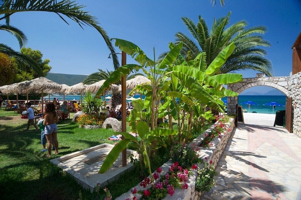 Un complexe hôtelier tropical doté d’une arche en pierre menant à la plage, d’une végétation luxuriante et de parasols en chaume.