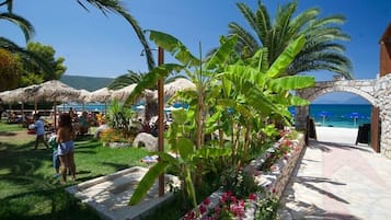 Un complexe hôtelier tropical doté d’une arche en pierre menant à la plage, d’une végétation luxuriante et de parasols en chaume.