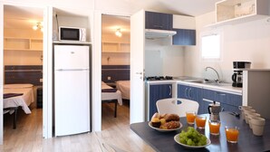 Een compacte keuken met een magnetron, koelkast en spoelbak. Een ontbijttafel met gebak, fruit en sinaasappelsap is zichtbaar.