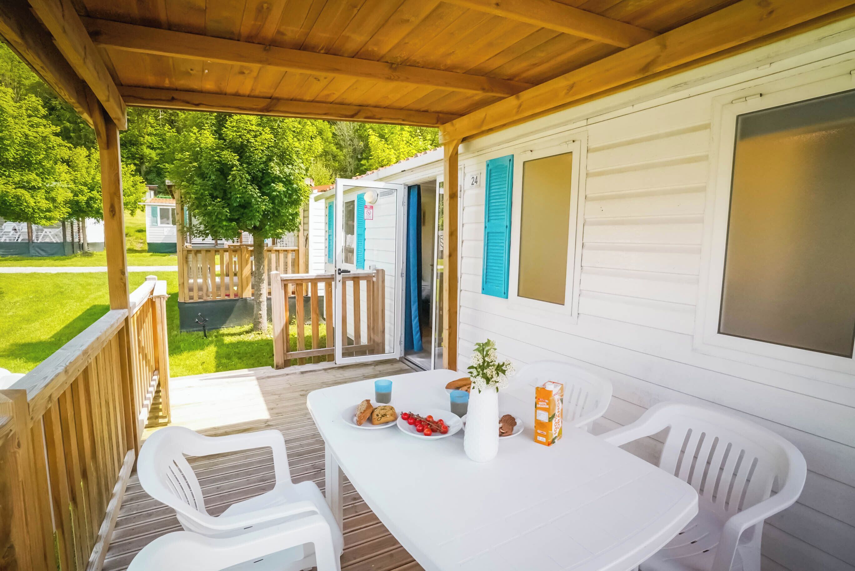 Un espace extérieur abrité, avec une table blanche dressée pour le repas, entourée de chaises en plastique blanches.