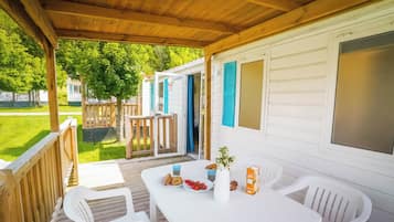 Un espace extérieur abrité, avec une table blanche dressée pour le repas, entourée de chaises en plastique blanches.