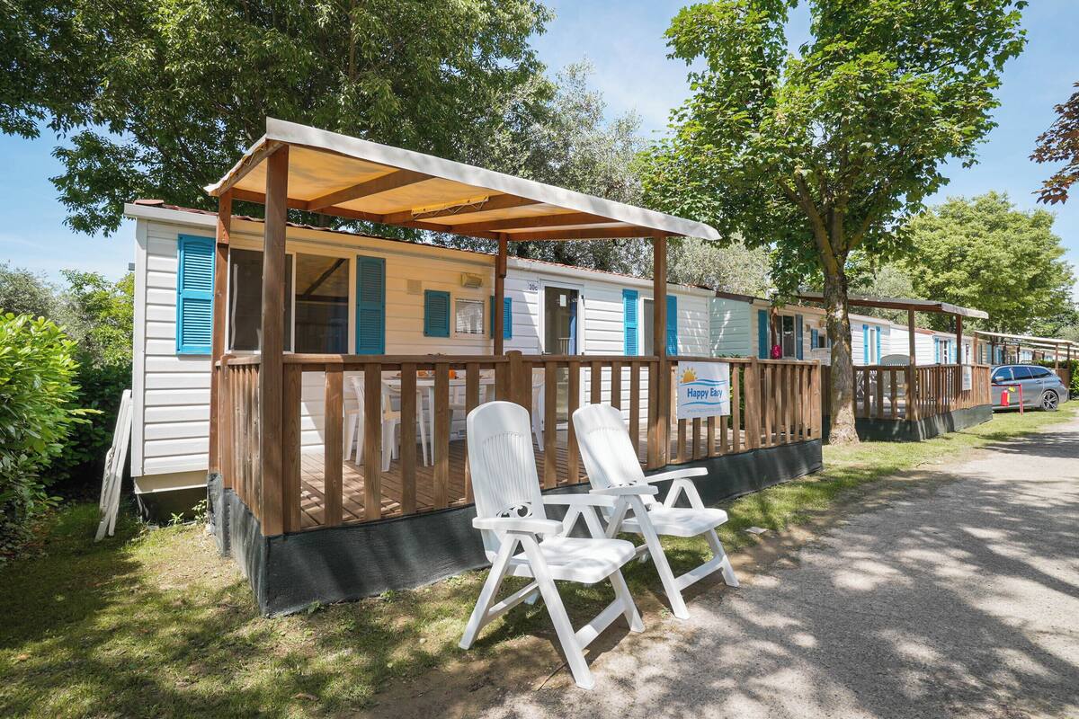 Une rangée de maisons mobiles dotées de terrasses en bois et de volets bleus, chacune ayant un petit porche et un espace salon extérieur.