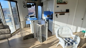 Un vaste espace de vie doté d’un haut plafond, une table à manger avec des chaises, un fauteuil en osier et une vue dégagée grâce à de grandes fenêtres.