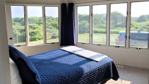 Une chambre avec un grand lit, de nombreuses fenêtres et une vue sur la verdure.
