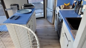Une cuisine de taille réduite avec un plan de travail bleu, des placards blancs et une vue par la fenêtre.
