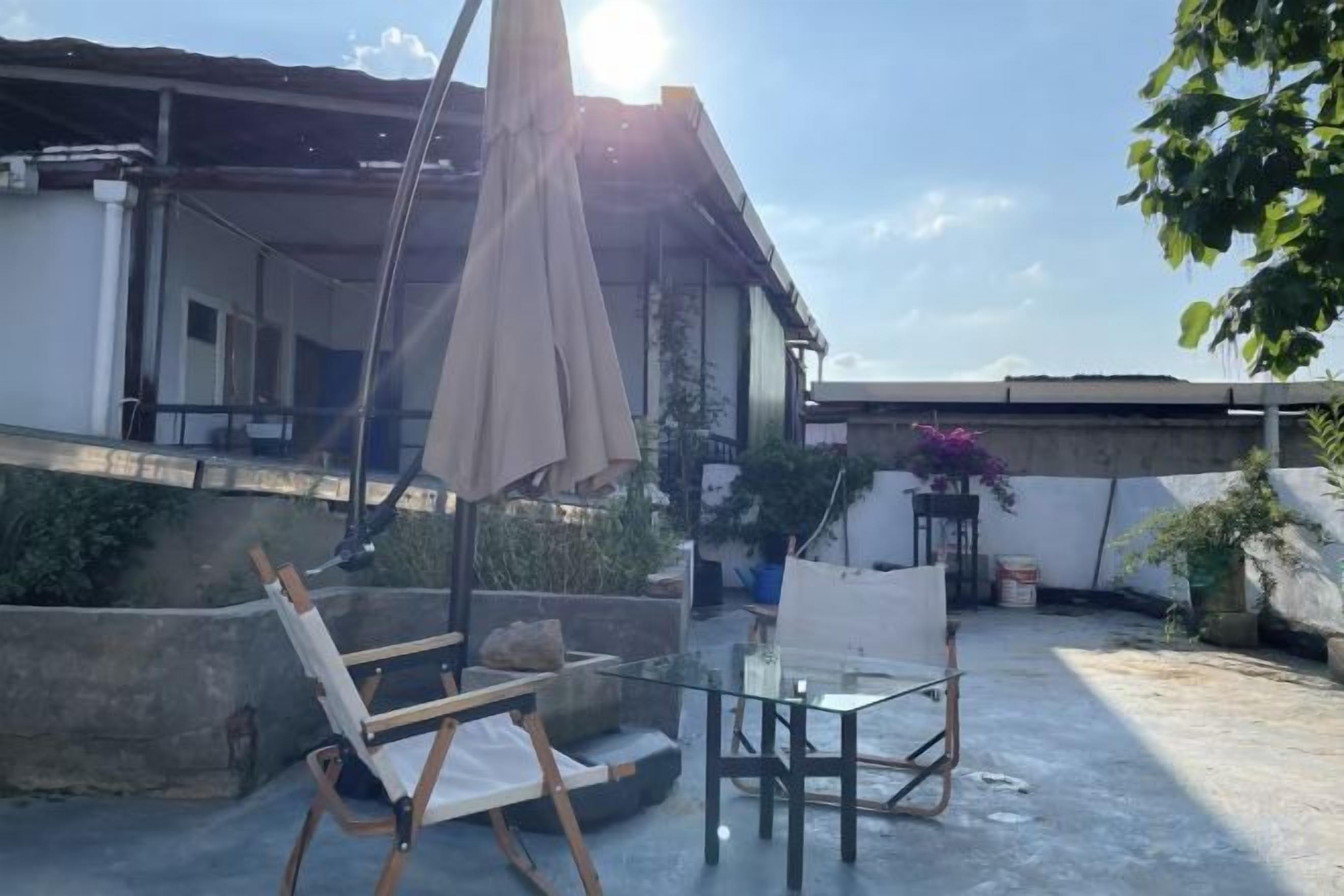 A rooftop terrace with a glass table, a folding chair, and a large umbrella.