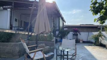 A rooftop terrace with a glass table, a folding chair, and a large umbrella.