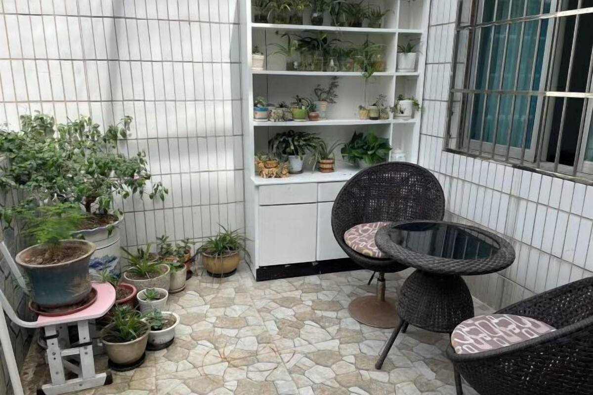 Ein kleiner Balkon mit Blumentöpfen, einem weißen Regalschrank und Korbstühlen.