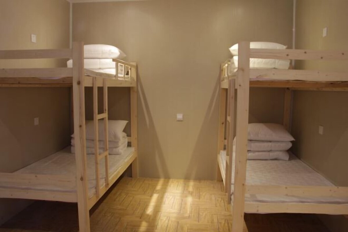 A room with two bunk beds, wooden flooring, and beige walls.
