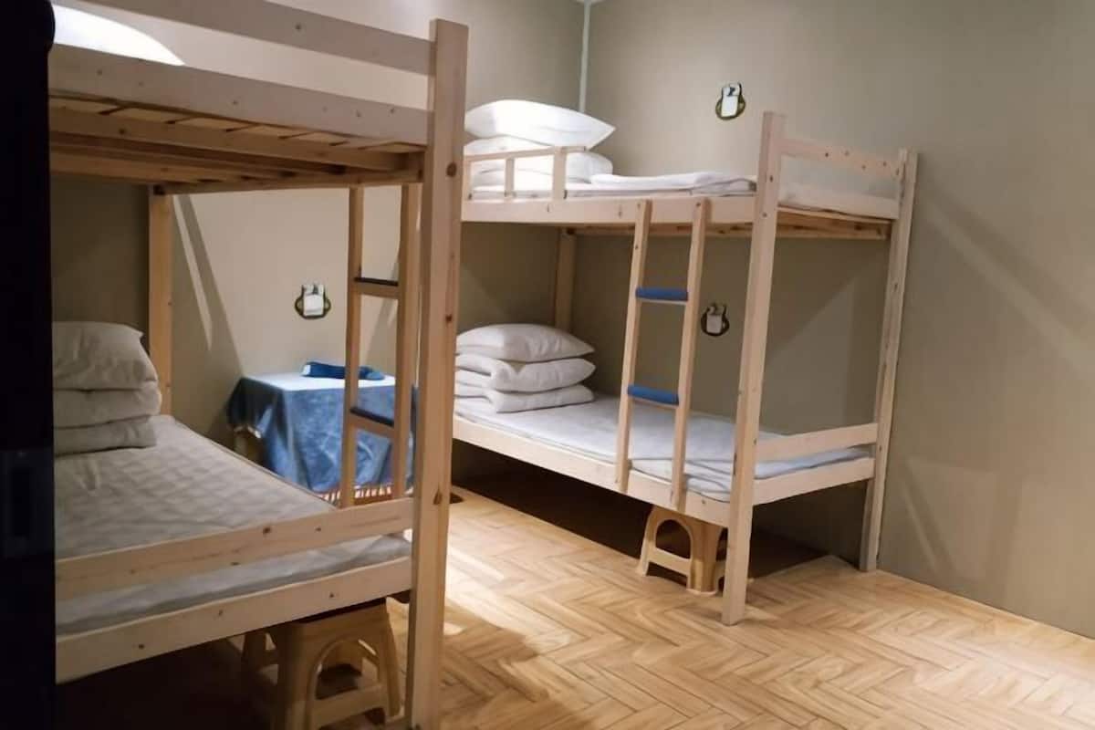 A bunk bed room with a wooden floor, a small table with a blue tablecloth, and a wall-mounted clock.