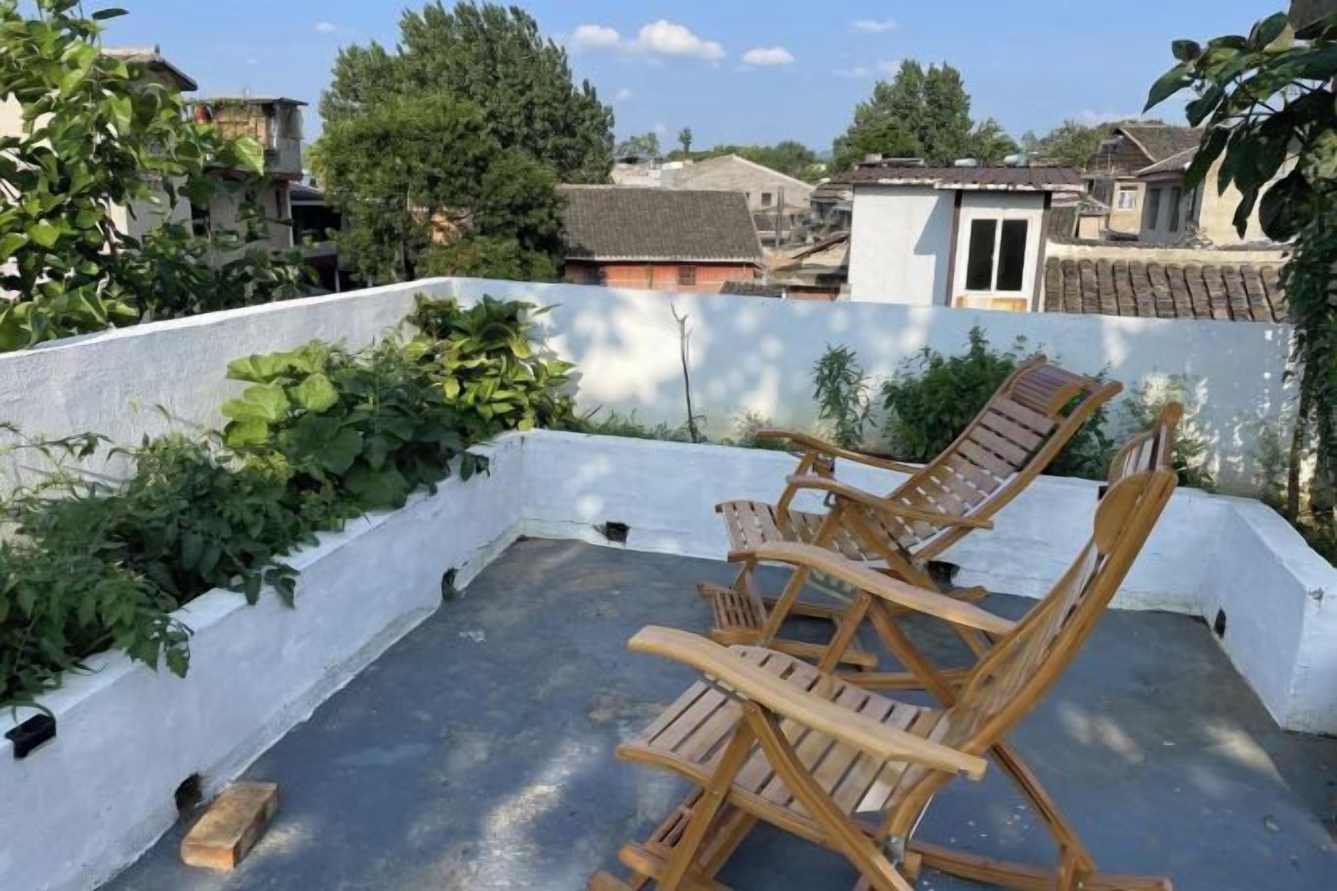 A rooftop terrace with wooden chairs and a white wall.