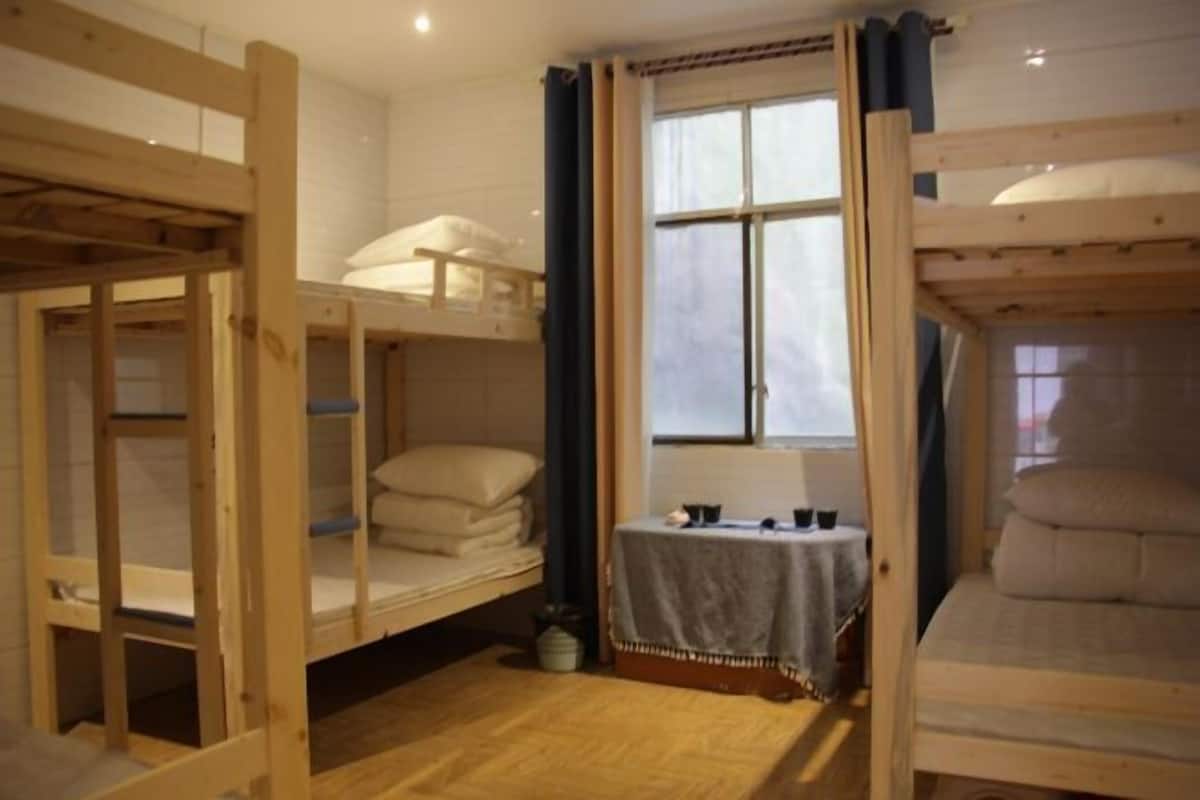 A room with bunk beds, a small table with a tablecloth, and a window with curtains.
