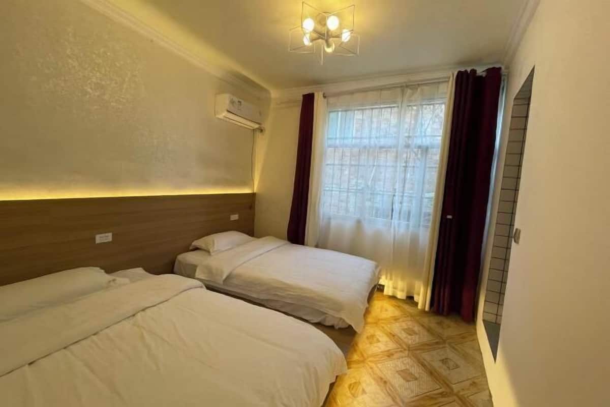 A hotel room with two beds, a wooden headboard, a ceiling light fixture, and a window with curtains.