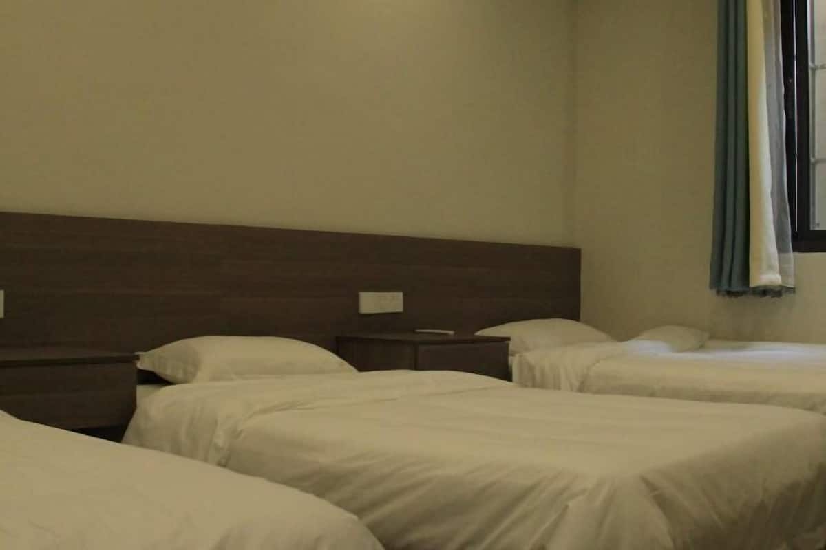 A hotel room with three single beds, wooden headboards, and a window with curtains.