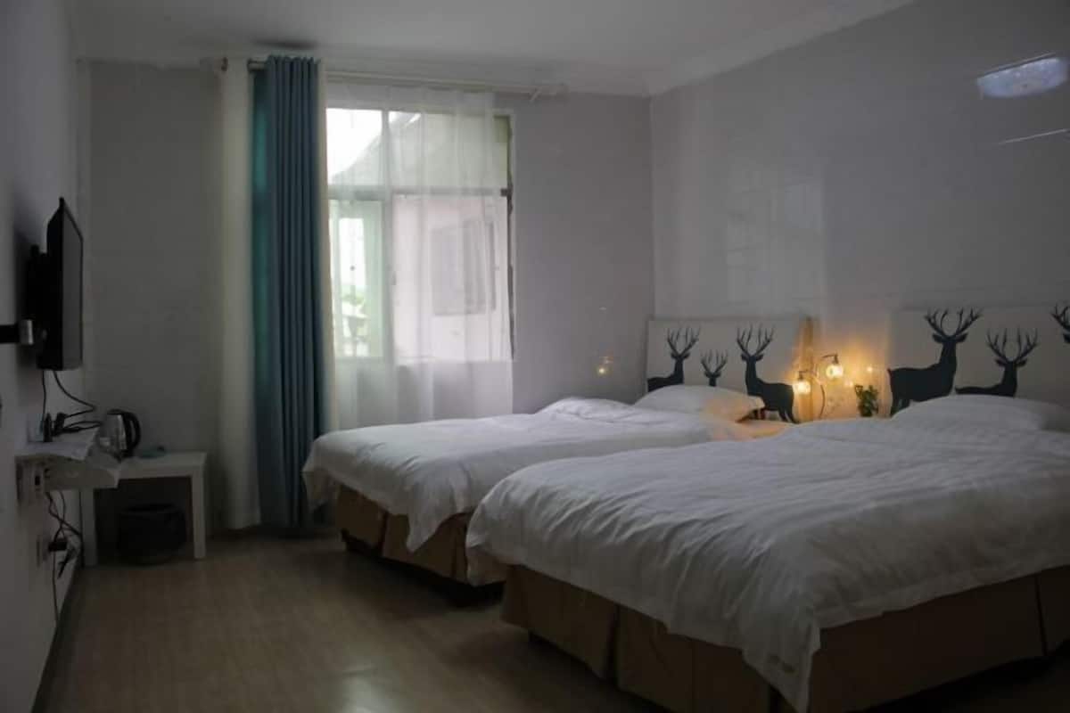 A hotel room with two beds, a TV, a small table, and a window with curtains.