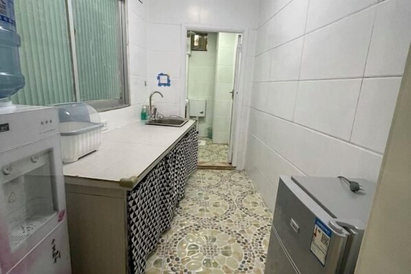 A small, narrow bathroom with white tiled walls and floor, a sink, a mirror, and a water dispenser. - Fangwu Youth Hostel (Guiyang)