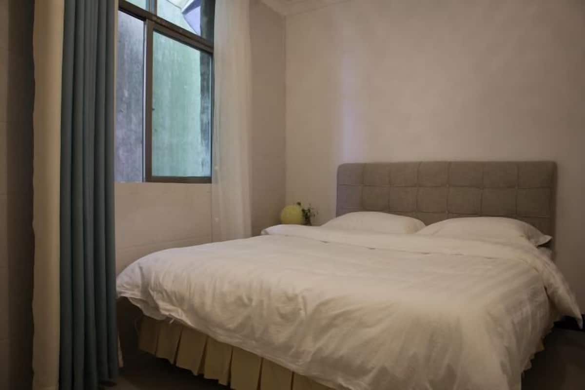 A bedroom with a bed, a window, and a curtain.