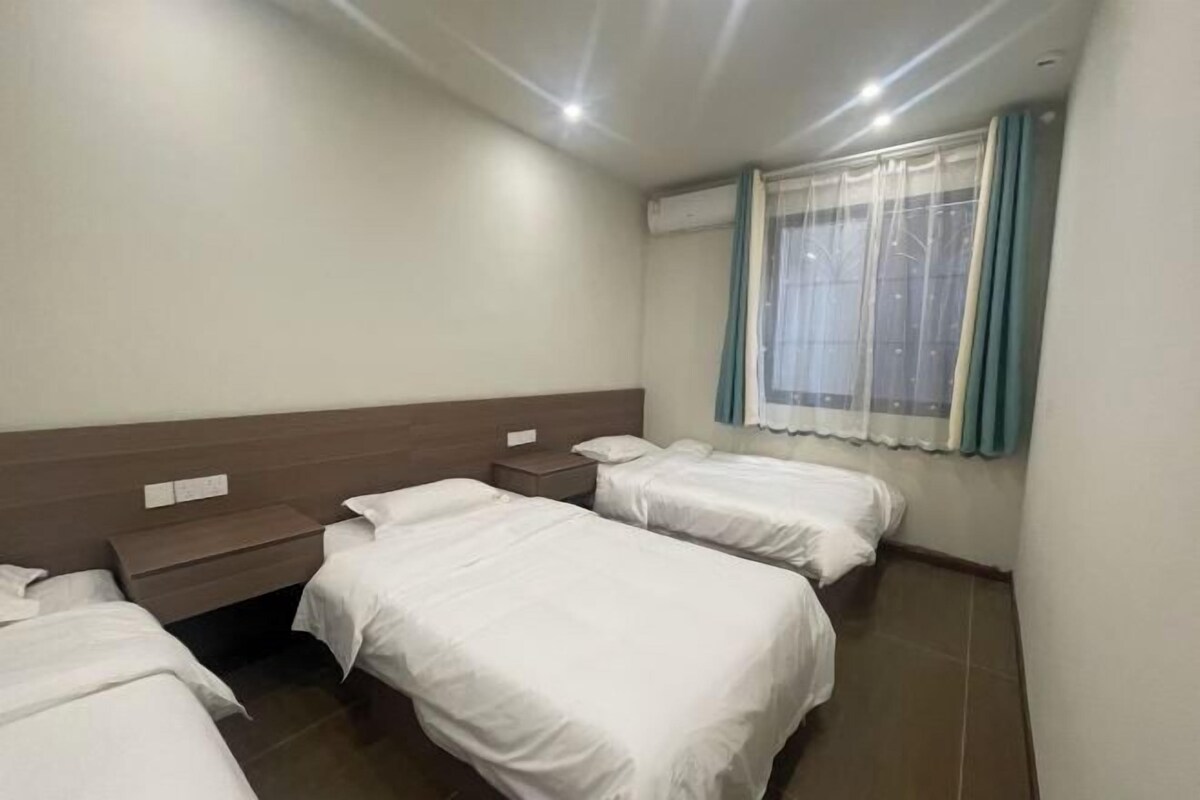 A hotel room with two single beds, a nightstand, a window with curtains, and a wall-mounted air conditioning unit.
