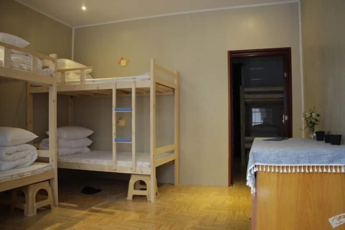 A room with bunk beds, a wooden desk, and a door leading to another room.