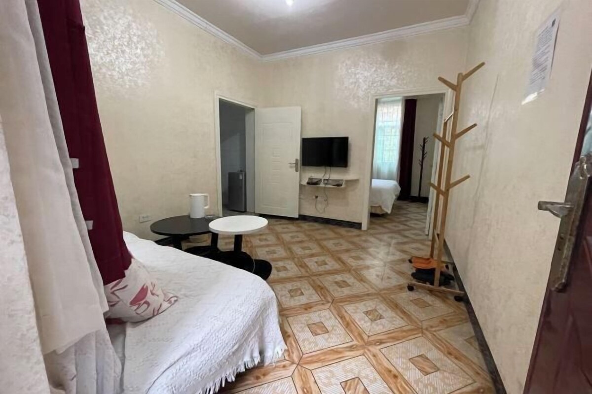 A hotel room with a bed, a small table, a TV mounted on the wall, and a wooden ladder leaning against the wall.