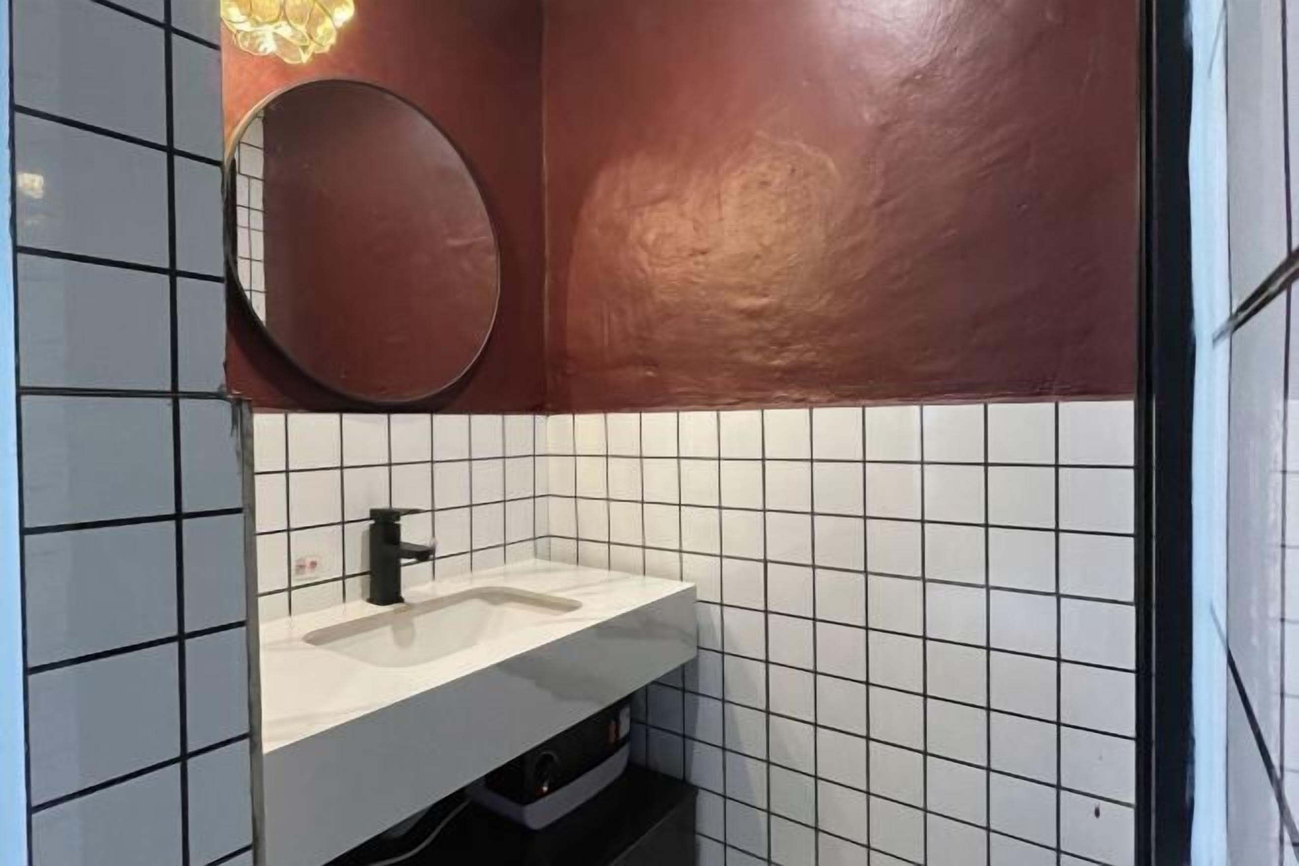 Un baño con lavamanos blanco, grifo negro y un espejo redondo en la pared.